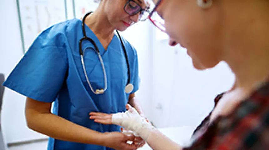Provider in blue scrubs bandaging patient's hand