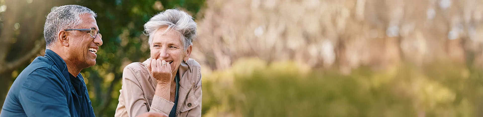 A happy older couple smiles and shares a laugh outdoors on a beautiful day.
