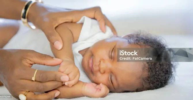 A baby peacefully sleeping on a soft surface, is being gently cared for by adult hands.