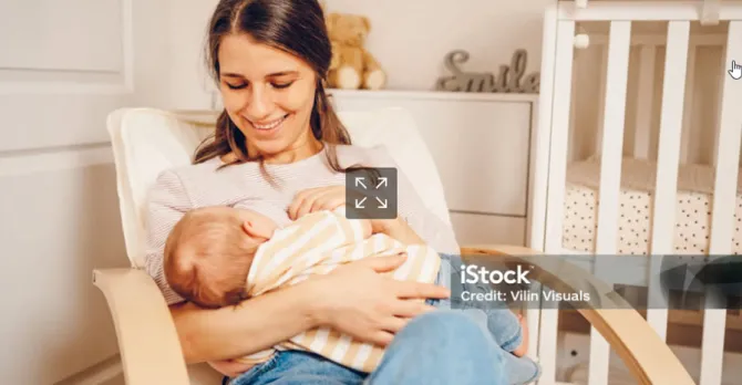 A mother sits in a chair in the baby's room while breastfeeding.