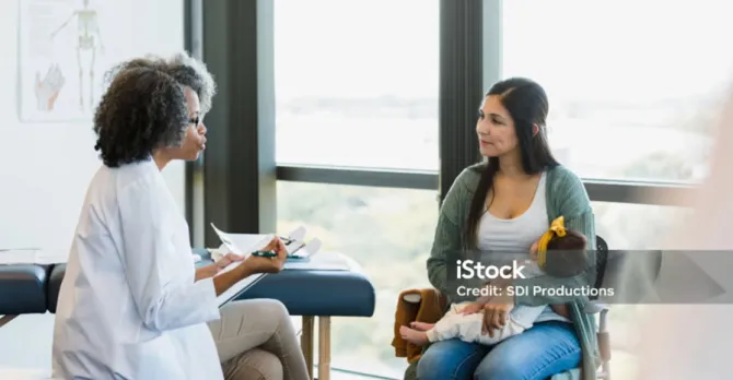 A new mom and her baby speak to a doctor in an exam room.