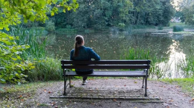 woman sitting on bench looking at trees and pond practicing mindfulness in nature