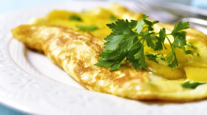 Omelet stuffed with potato and vegetables on a white plate on blue wooden background
