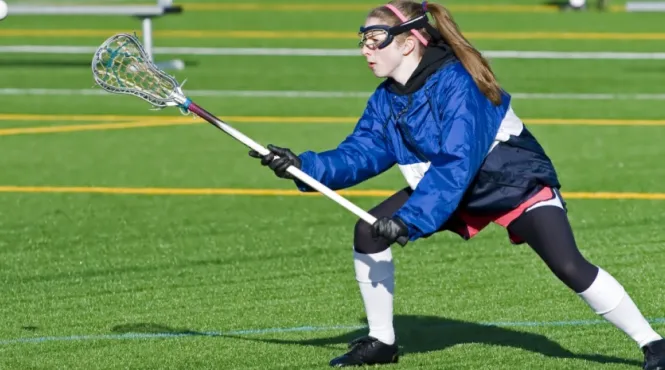 Teen girl playing lacrosse on a green field