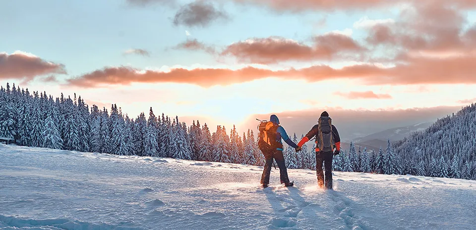 Two people holding hands hiking over snow