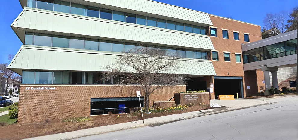 A red brick building with green awnings on each floor, against a blue sky. 33 Kendall Street is on the side of the building of the Peter H Levine Ambulatory Center at UMass Memorial Medical Center - Memorial Campus.