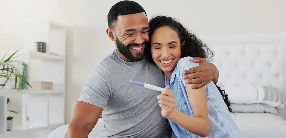 A couple rejoices in an embrace while looking at the results of a pregnancy test.
