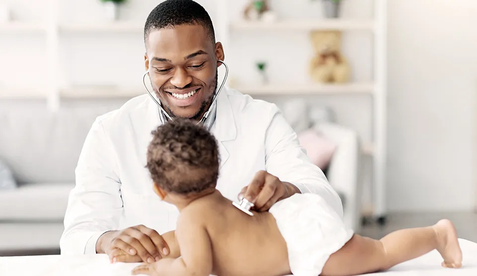 A smiling doctor examining a baby on a table.