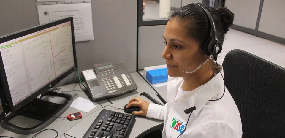 A woman sits at a desk in a medical office, using a telephone headset and her computer.