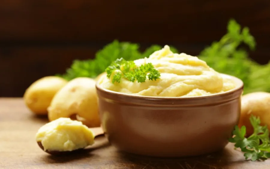 a brown bowl with vegan mashed potatoes and parsley and raw potatoes next to it.