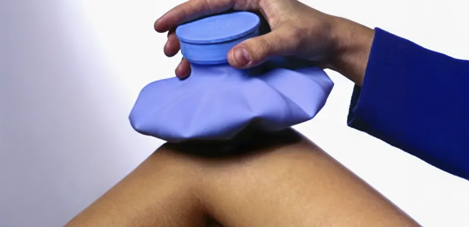 Someone's hand is holding a blue ice bag in place on their bent knee.