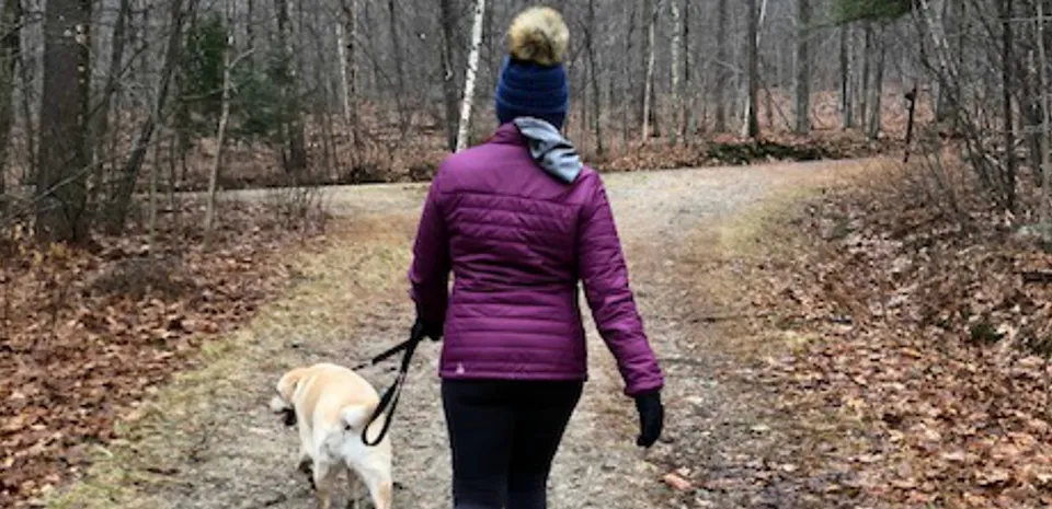 woman walking dog down trail in woods