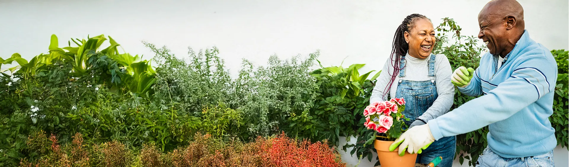 A black woman and man smile and laugh as they garden together.