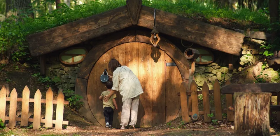 child and adult looking at a hobbit house in the woods.