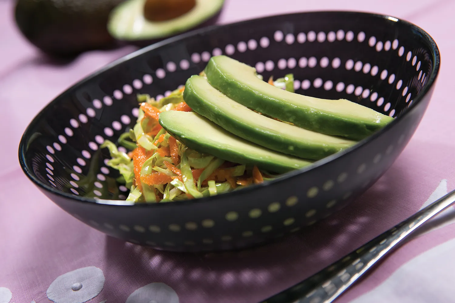 A black bowl with a salad topped with avocado.