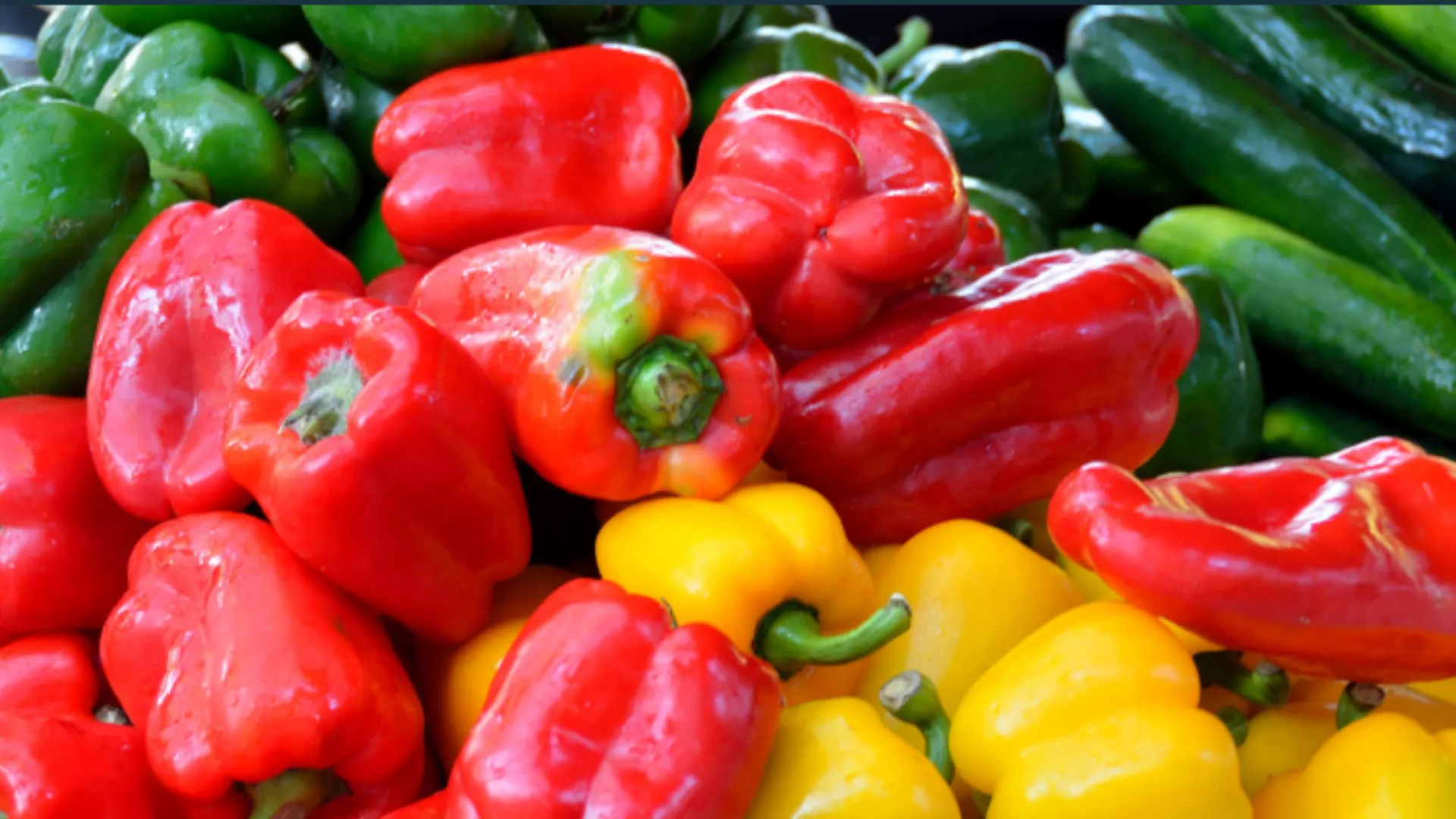 Red and yellow peppers are on a pile of other vegetables.