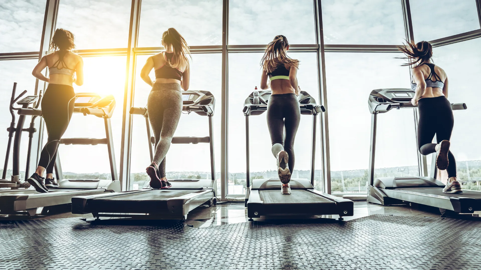 Multiple women are shown on treadmills from behind.