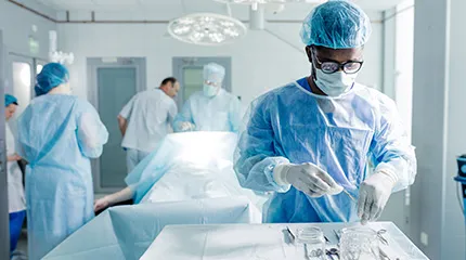 A caregiver sets up a table of surgical instruments in an operating room.