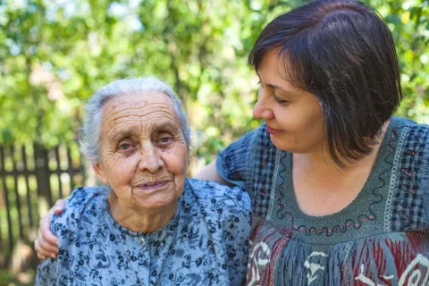 Loving daughter puts arm around elderly mother as she avoids caregiver burnout