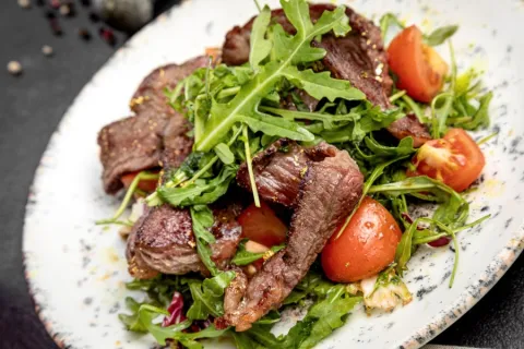 New York strip steak salad with steak on a bed of lettuce on a white plate