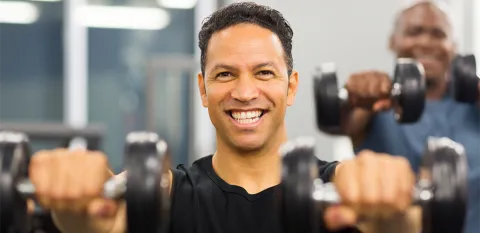 Two men doing shoulder exercises with dumbbells at the gym.