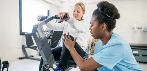 A nurse helps a patient on an exercise machine as part of her rehabilitation therapy.