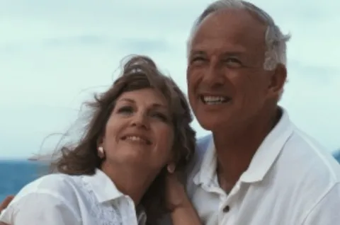 A couple looks toward the horizon while the woman leans back into her partner's shoulder.