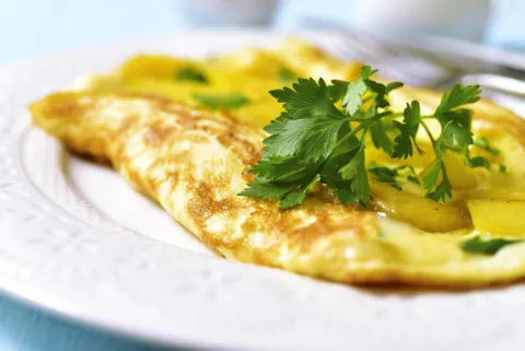Omelet stuffed with potato and vegetables on a white plate on blue wooden background
