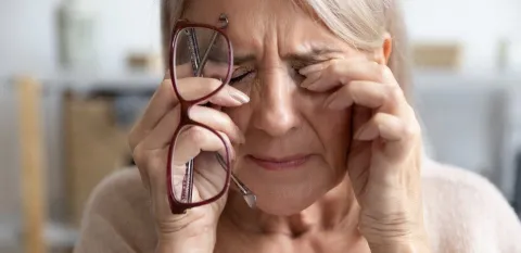 A mature woman holds her glasses and rubs her eyes.
