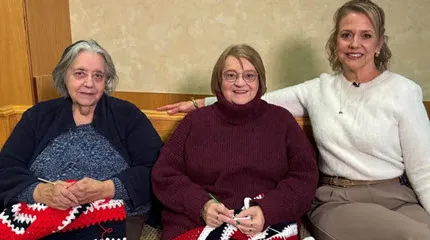 Adrienne Renaud and her younger sister, Rosemarie Frechette sit with Reverent Renee Anderson while crocheting the red, white, and blue shawls, 