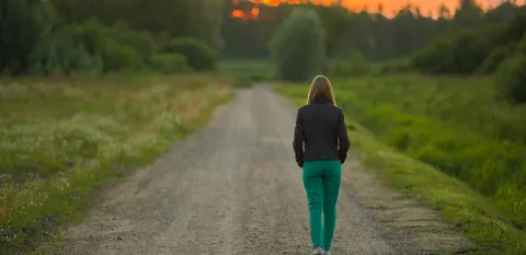 woman walking down a dirt road towards the sunset