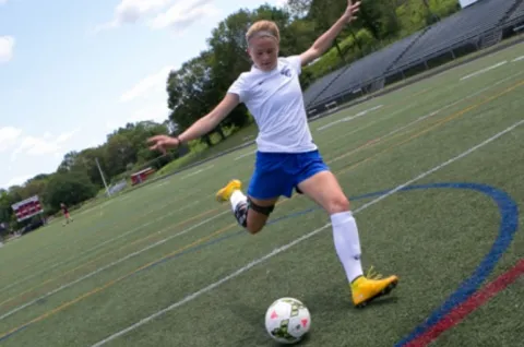 An athlete is kicking a soccer ball on a large field.
