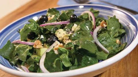A blue bowl with a salad made of spinach, avocado, blueberries, onions, and chia seeds.