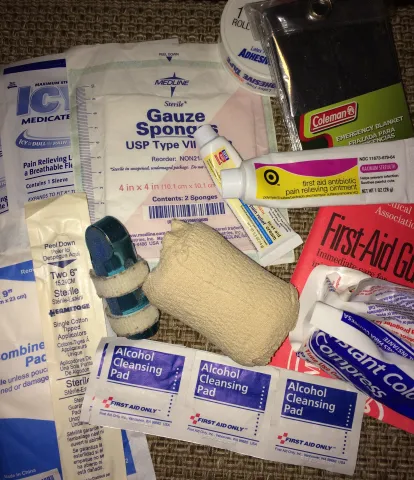 A closeup shows various medical supplies in a first aid kit, including gauze, ointments, and bandages.