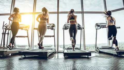 Multiple women are shown on treadmills from behind.