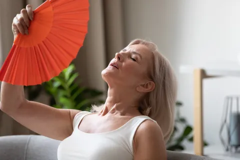 A mature woman is fanning herself with a red hand fan.