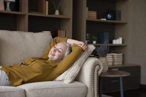 A woman in a yellow shirt is laying on a couch with her arms above her head.