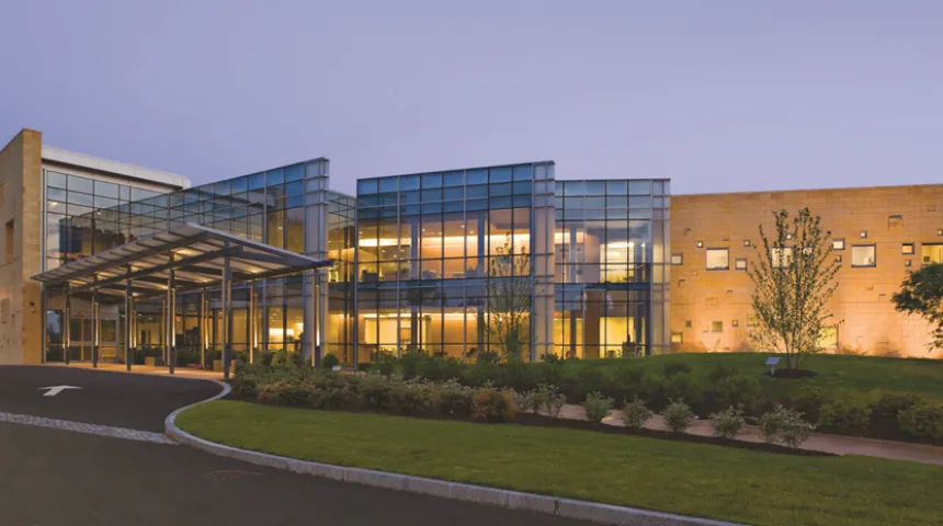 The Cancer Center at night. The front of the building features many glass panes while the lights are on inside.