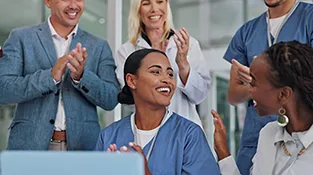 Woman smiles as her colleagues stand around her clapping