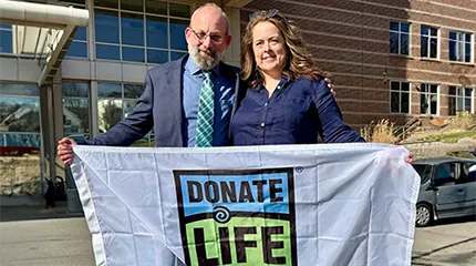 Erin Murphy and Keith Baldinger stand arm-in-arm, holding a Donate Life banner together.