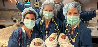 A team of very happy nurses at UMass Memorial Medical Center are holding newborn, swaddled triplets. 