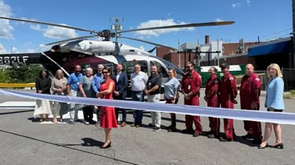 A group of people stand in front of a helicopter at a ribbon-cutting ceremony.