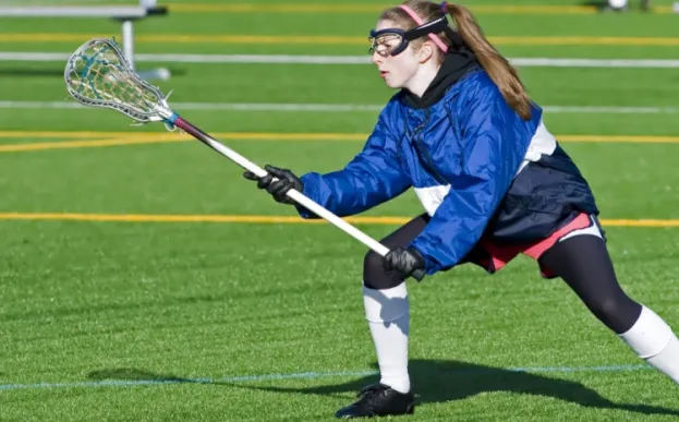Teen girl playing lacrosse on a green field