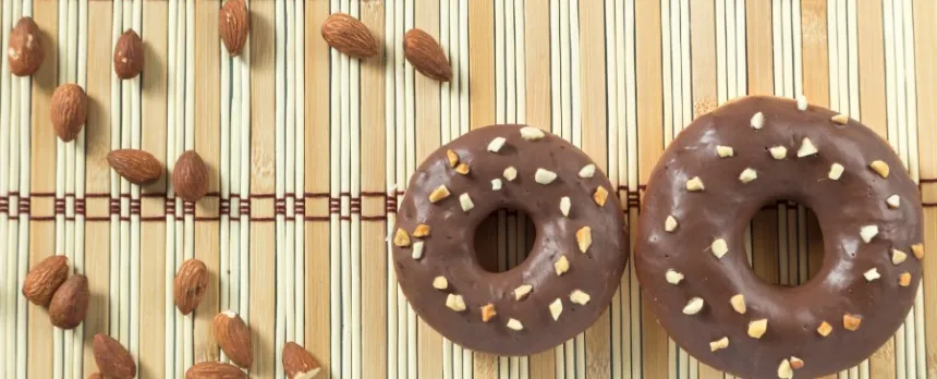 Two Avocado-Dark Chocolate Glazed Donuts with almonds on a bamboo placemat.