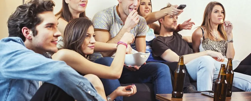 A college age group of teens are drinking and watching tv.