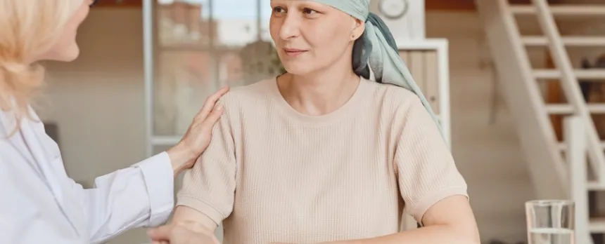 Woman with cancer wearing head cover is comforted by an oncology nurse navigator