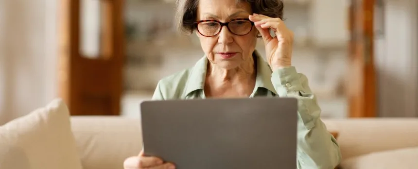older woman with cataracts wearing glasses struggling to look at a computer.
