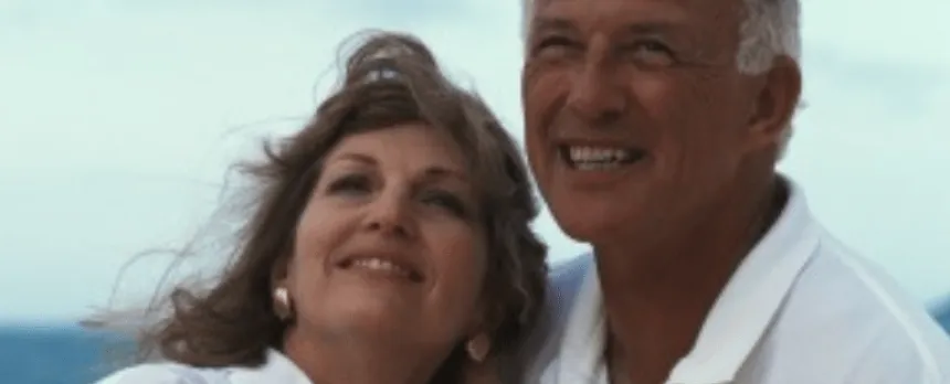 A couple looks toward the horizon while the woman leans back into her partner's shoulder.