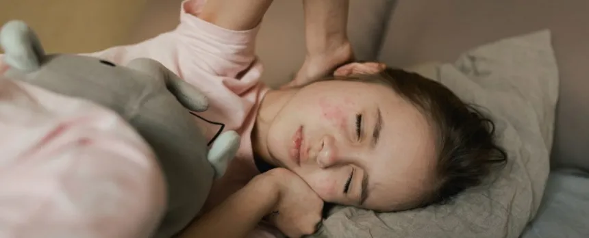 young girl with measles lying in a bed with eyes closed