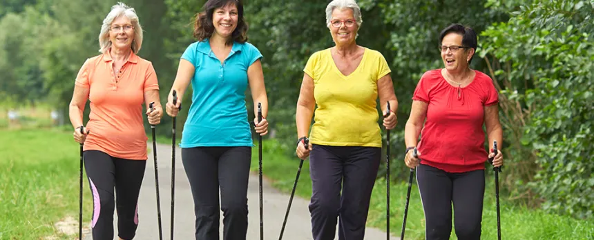 A group of mature women with hiking sticks are walking on a path.